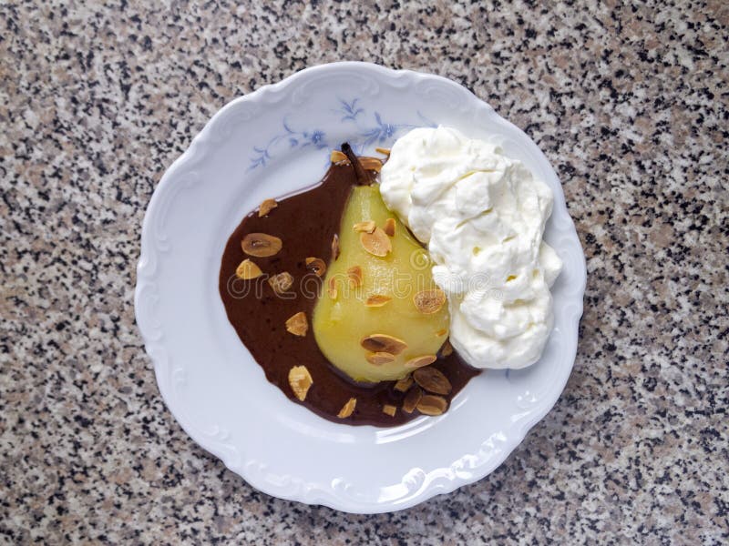 Top view of one poached pear with whipped cream, chocolate sauce and almond flakes. French dessert poire belle Helene