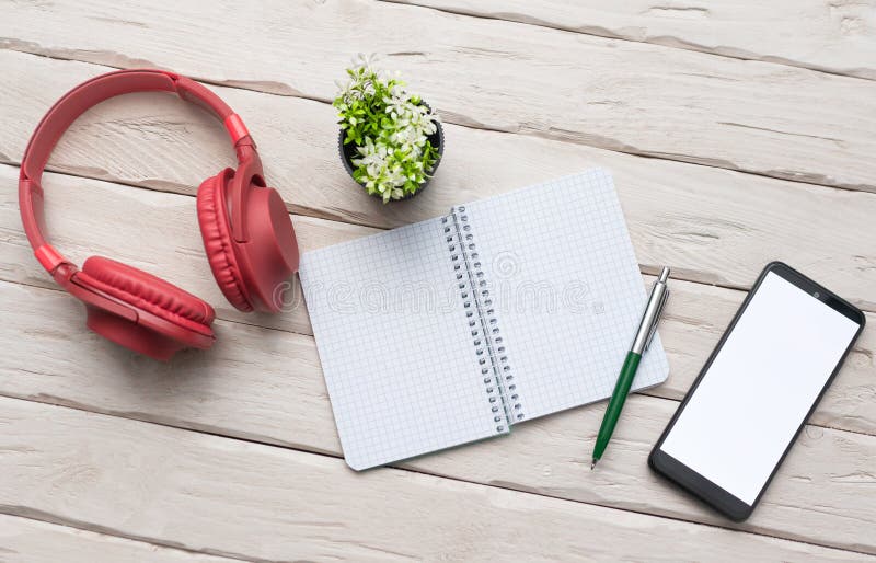 Top view Over-ear red headphones with a smartphone with a white display. Headphones with notepad and writing pen. Desktop. Online royalty free stock photo