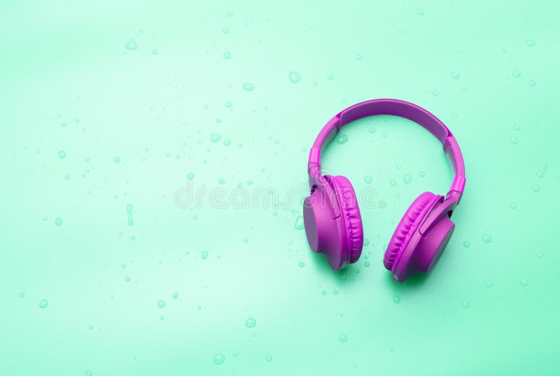 Top view Purple overhead music headphones in water drops, copy space. Headphones on a pastel green background on a wet surface. stock photos