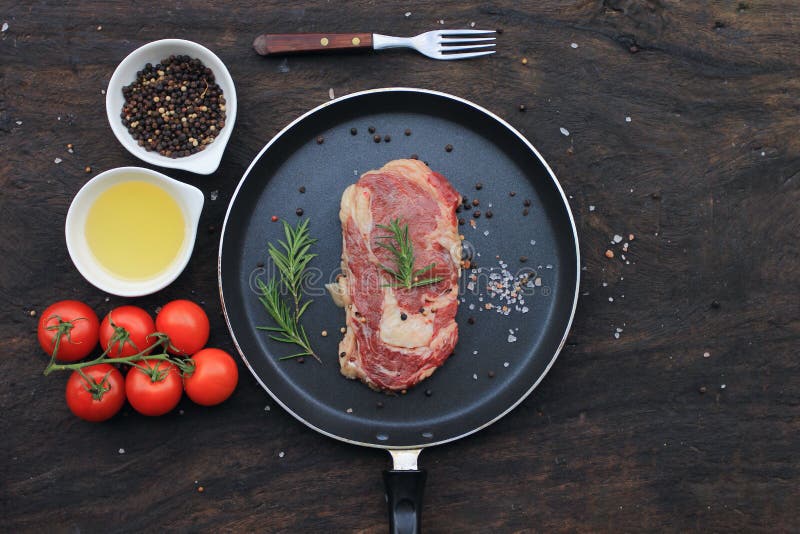 Top view of Raw beef steak with rosemary in frying pan and vegetables on wooden dark background, food meat or barbecue royalty free stock photo Top view of Raw beef steak with rosemary in frying pan and vegetables on wooden dark background, food meat or barbecue royalty free stock photo