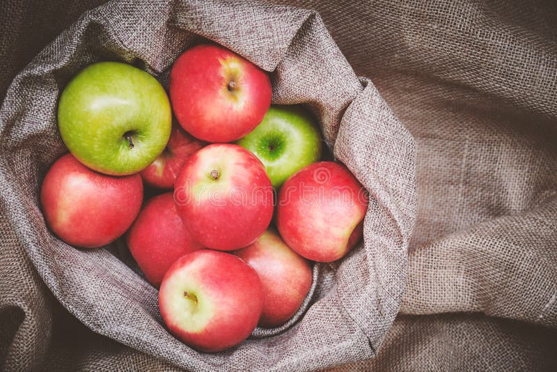 Red apples, green apples in basket cover with brown burlap background texture stock photo