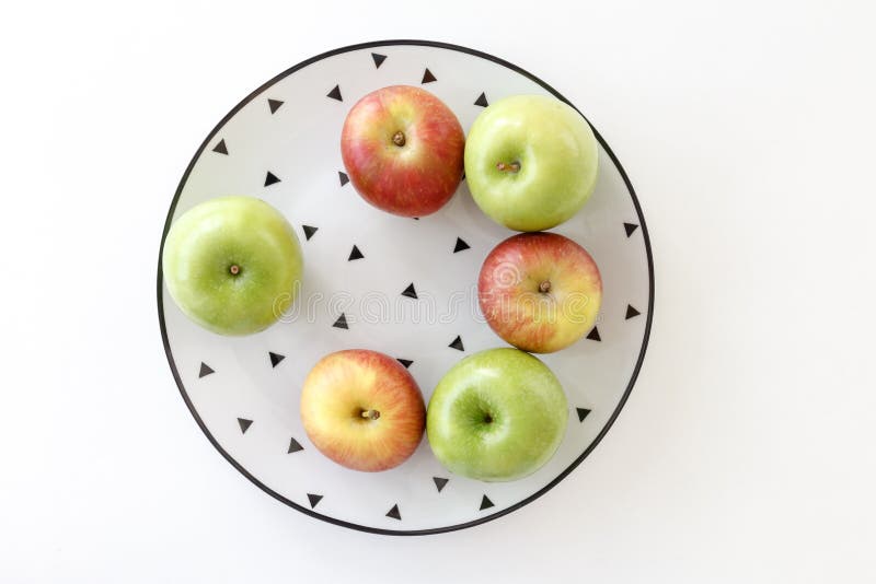 Top view of Red and green apples in white plate with black triangles pattern on white background