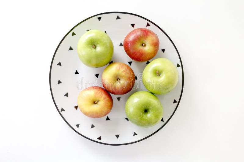 Top view of Red and green apples in white plate with black triangles pattern on white background