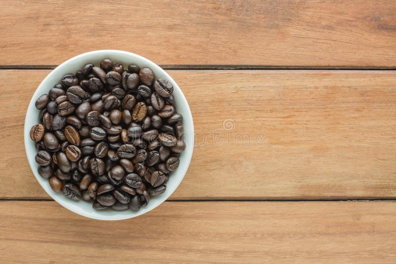 Roasted dark coffee beans in bowl on wooden background