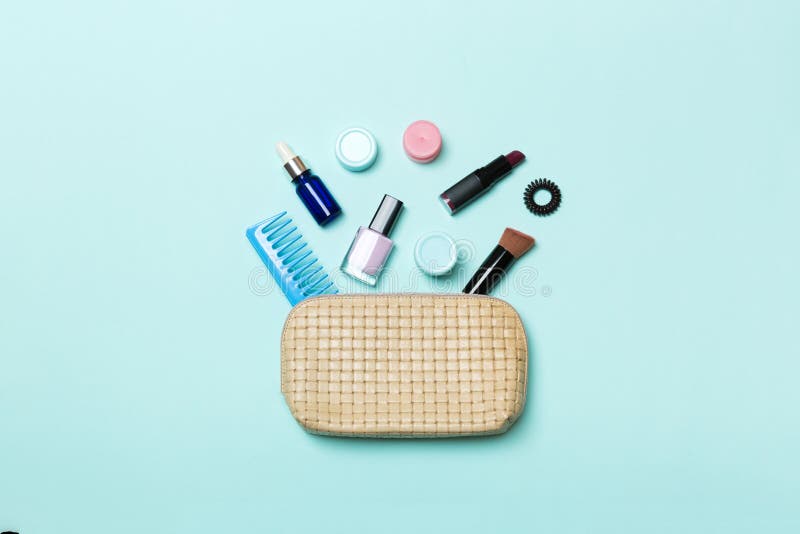 Top view of set of make up and skin care products spilling out of cosmetics bag on blue background. Beauty concept