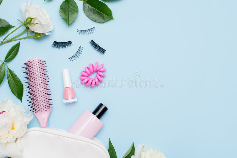 Top view of set of make up and skin care products spilling out of cosmetics bag on blue background with white flowers and copy