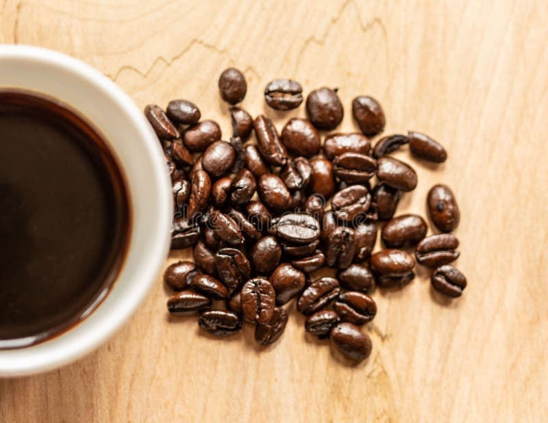 Top View Shot of a Bunch of Coffee Beans and a Half Full Coffee Cup