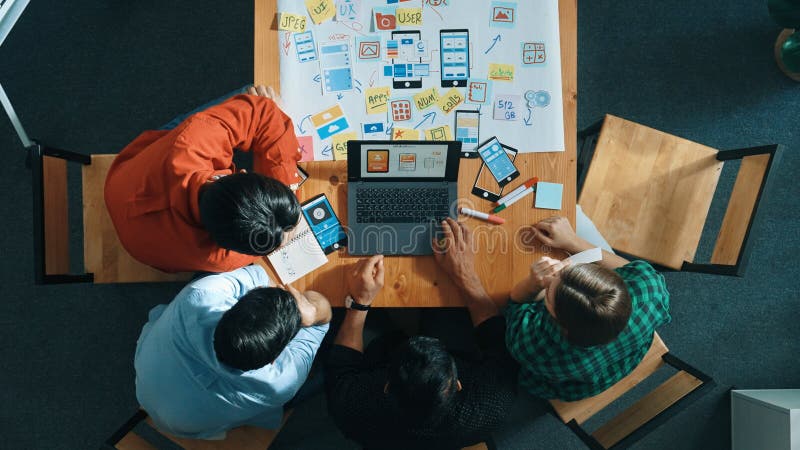 Top view of skilled manager using laptop working on Ux Ui design. Convocation. Top view of project manager using laptop working on Ux Ui design for mobile phone interface while marketing team designing software program by using brainstorming mind map. Top view.