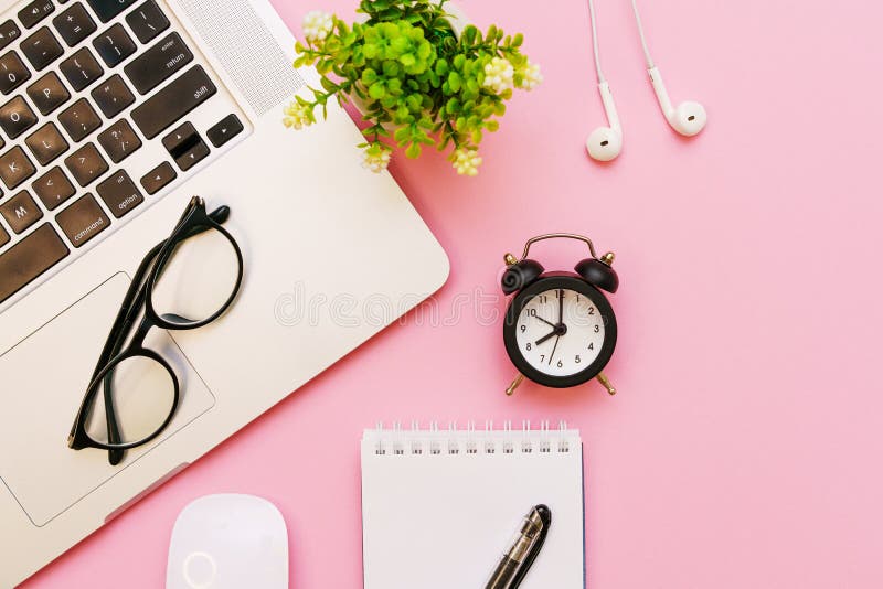 Alarm clock and glasses, white wired headphones and laptop on pink background.