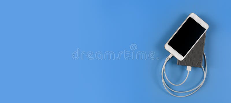 Top view smartphone charging with power bank on blue background with copy space. Smartphone charging with power bank by white USB stock photo