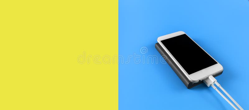 Top view smartphone charging with power bank on blue and empty yellow background with copy space. Smartphone charging with power stock photo