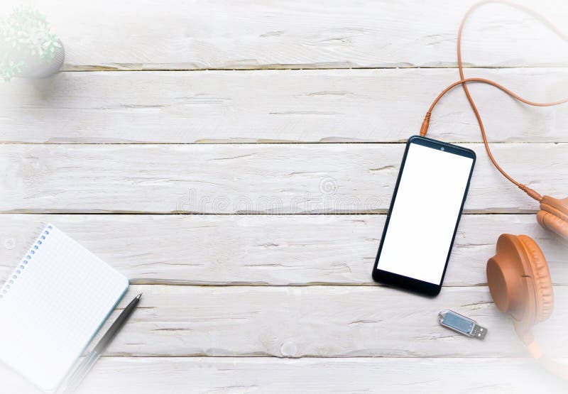 Top view Smartphone with white display, with headphones on a wooden table. On-ear headphones with a memory card, with a notepad royalty free stock photography