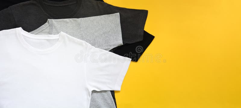 Top view stack of black, grey and white monochrome t-shirt on yellow background with copy space, flat lay royalty free stock image