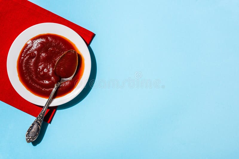 Top view of tasty tomato sauce in plate with spoon on red napkin on blue surface stock images