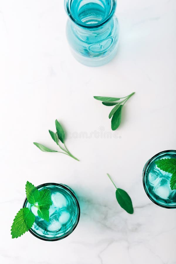 Top view of two beautiful vintage turquoise glasses and a bottle with cold drink and ice cubes, decorated with fresh green mint stock images Top view of two beautiful vintage turquoise glasses and a bottle with cold drink and ice cubes, decorated with fresh green mint stock images