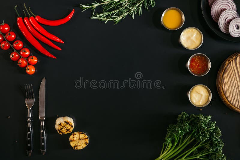 top view of various sauces, grilled garlic, fork with knife and fresh vegetables with herbs