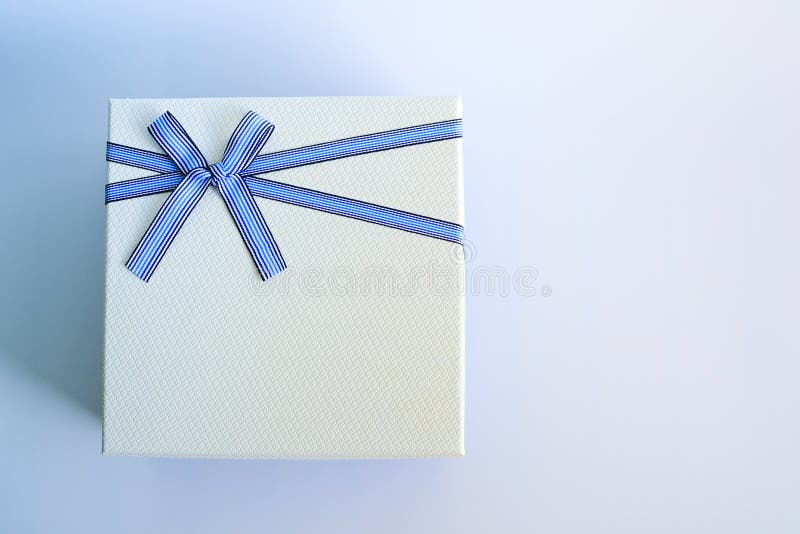 Top view of white gift box or present box package with a blue ribbon and bow on a blue and white background.