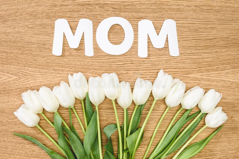 top view of white tulips and word mom on wooden table, mothers day concept