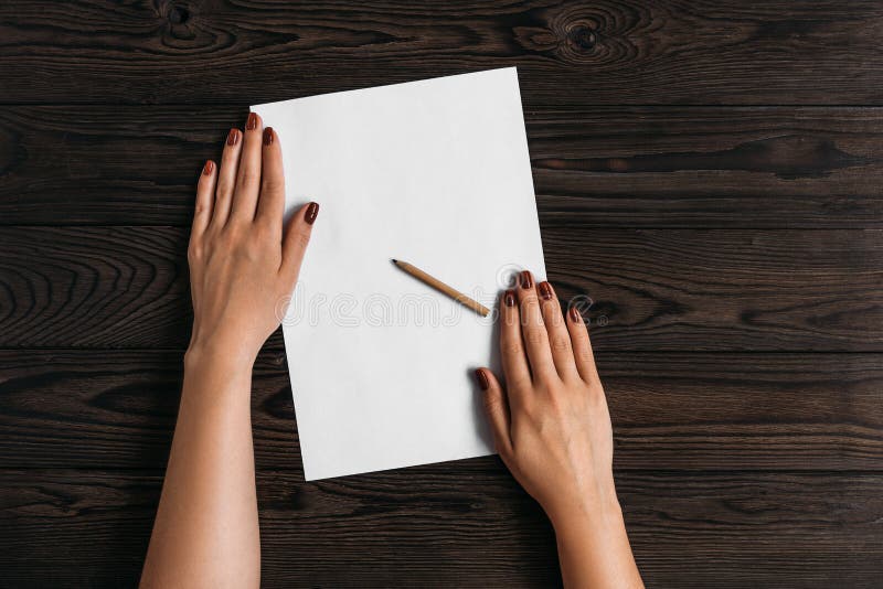 Top view of women`s hands, ready to write something on an empty piece of paper lying on a wooden table. White blank sheet of pape stock photography Top view of women`s hands, ready to write something on an empty piece of paper lying on a wooden table. White blank sheet of pape stock photography