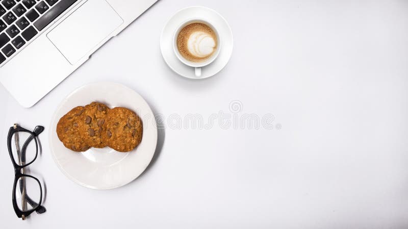 Top view of work place table, laptop with glasses cookies and cup of cappuccino on white background