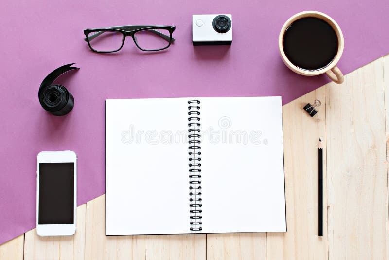 Top view of working desk with blank notebook with pencil, coffee cup, eyeglasses, mobile phone and action camera on wooden backgro