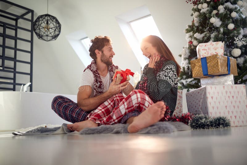 Top view of young beardy guy surprising his girlfriend with Christmas present while having breakfast in bed together