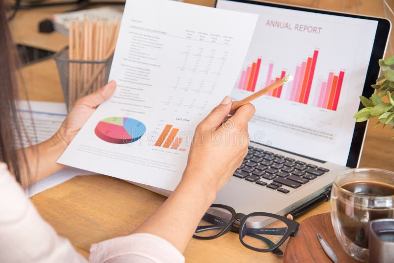 Top View Of Young Working Woman Using Laptop And Reading Annual Report Document At Work. Business Woman Working At Her Desk