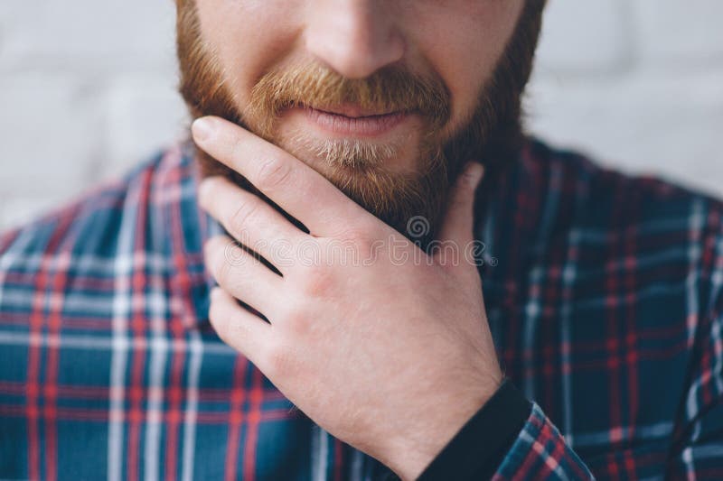 Young man in a flannel shirt touches with hand his beard. Young man in a flannel shirt touches with hand his beard