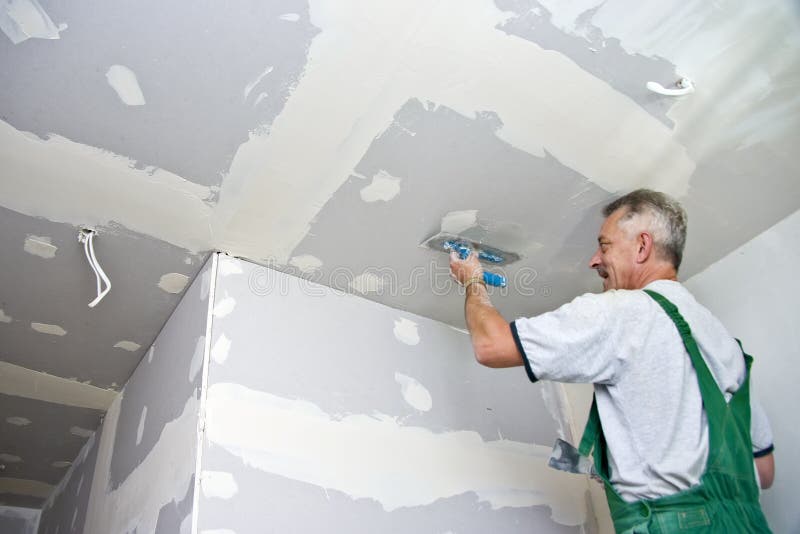 A smiling dry waller standing on a ladder high at the ceiling, putting plaster on the walls with a special tool. A smiling dry waller standing on a ladder high at the ceiling, putting plaster on the walls with a special tool.