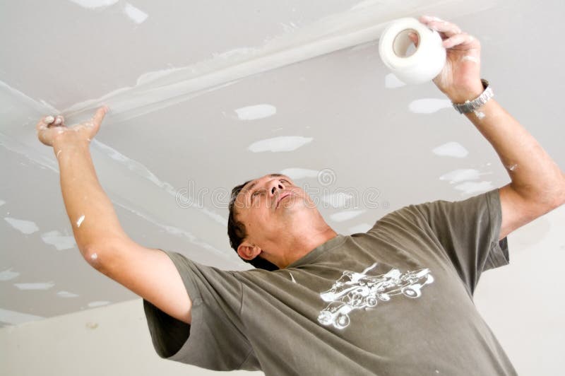 A dry waller standing on a ladder high at the ceiling, putting special tape on the joint. A dry waller standing on a ladder high at the ceiling, putting special tape on the joint.