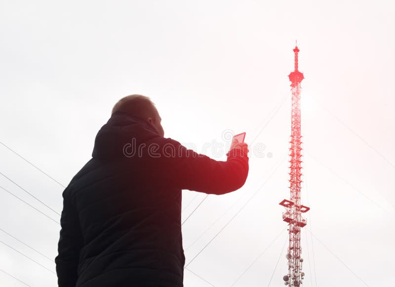 Torre móvil de la cual hay radiación y un hombre con un teléfono móvil, red pobre, modulación de la alta telecomunicación imagen de archivo Torre móvil de la cual hay radiación y un hombre con un teléfono móvil, red pobre, modulación de la alta telecomunicación imagen de archivo