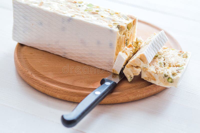 Torrone o turrón italiano con las almendras en una tabla de madera blanca, cierre para arriba con el foco seleccionado imagen de archivo Torrone o turrón italiano con las almendras en una tabla de madera blanca, cierre para arriba con el foco seleccionado imagen de archivo