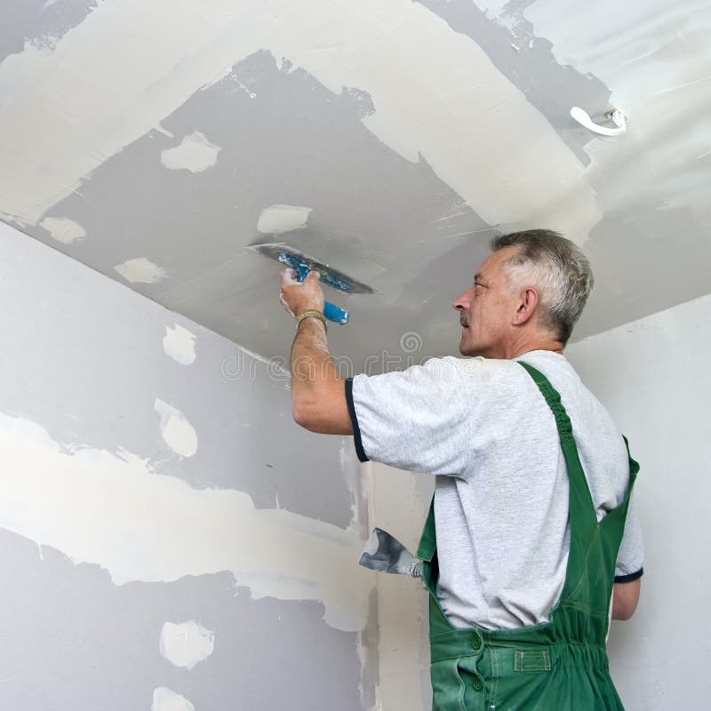 A dry waller standing on a ladder high at the ceiling, putting plaster on the walls with a special tool. A dry waller standing on a ladder high at the ceiling, putting plaster on the walls with a special tool.