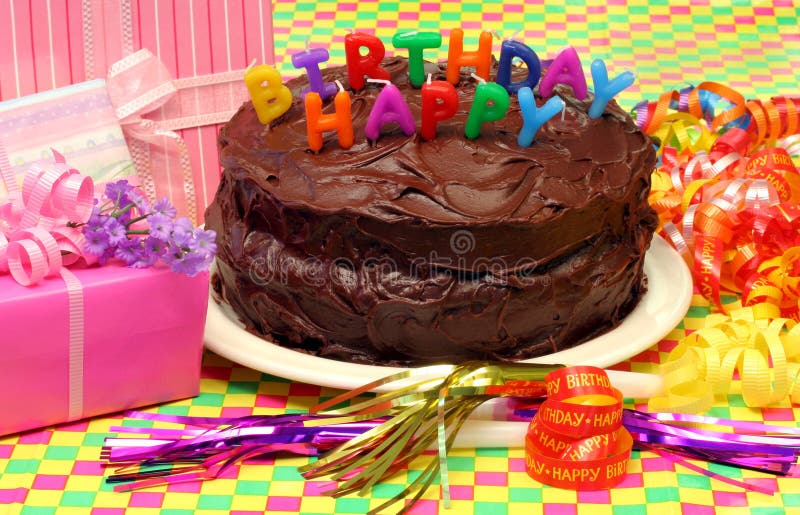 Chocolate Birthday Cake with Happy Birthday Candles and festive party supplies and gifts all around. Colorful and cheerful. Chocolate Birthday Cake with Happy Birthday Candles and festive party supplies and gifts all around. Colorful and cheerful.