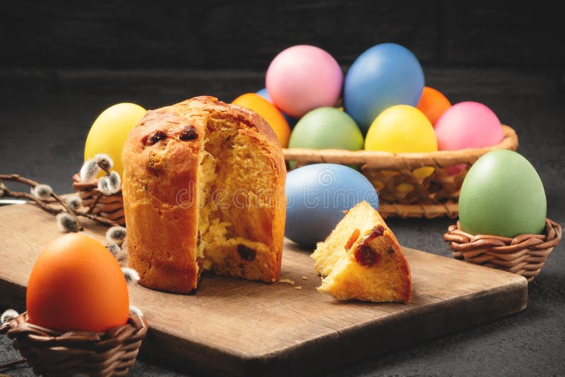 Torta pasquale su un tavolo da taglio e uova colorate su un tavolo e in un cestino di vimini - tradizionale colazione di Pasqua immagine stock Torta pasquale su un tavolo da taglio e uova colorate su un tavolo e in un cestino di vimini - tradizionale colazione di Pasqua immagine stock