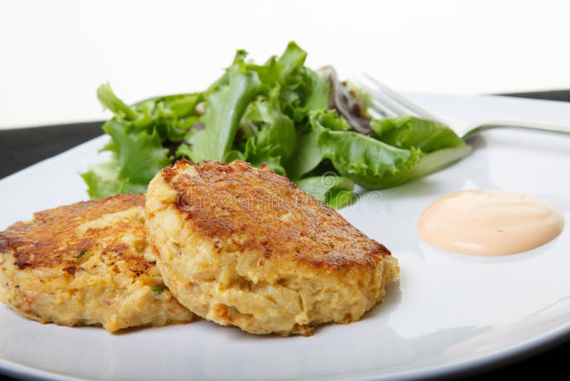 Fresh crab cakes on a white plate with sauce and a salad of field greens. Fresh crab cakes on a white plate with sauce and a salad of field greens