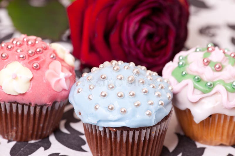 Macro picture of multi coloured cup cakes on the background with the red rose. Macro picture of multi coloured cup cakes on the background with the red rose.