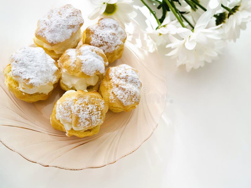 Cream puffs and eclairs cakes with filling, powdered sugar topping, chamomile flowers. Cream puffs and eclairs cakes with filling, powdered sugar topping, chamomile flowers