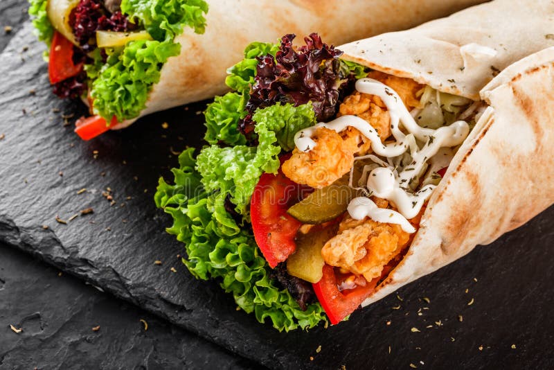 Tortilla opakunki z piec na grillu kurczakiem przepasuj?, ?wiezi warzywa i sa?atka na czer? kamienia tle Zdrowa przek?ska lub odd obraz stock Tortilla opakunki z piec na grillu kurczakiem przepasuj?, ?wiezi warzywa i sa?atka na czer? kamienia tle Zdrowa przek?ska lub odd obraz stock