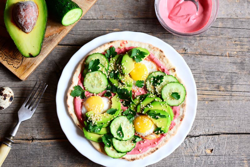Tortilla wypiętrzał wysoko z, lathered z beetroot hummus, i smażącymi przepiórek jajkami, avocado, ogórkami, sezamem i pietruszką obraz royalty free Tortilla wypiętrzał wysoko z, lathered z beetroot hummus, i smażącymi przepiórek jajkami, avocado, ogórkami, sezamem i pietruszką obraz royalty free