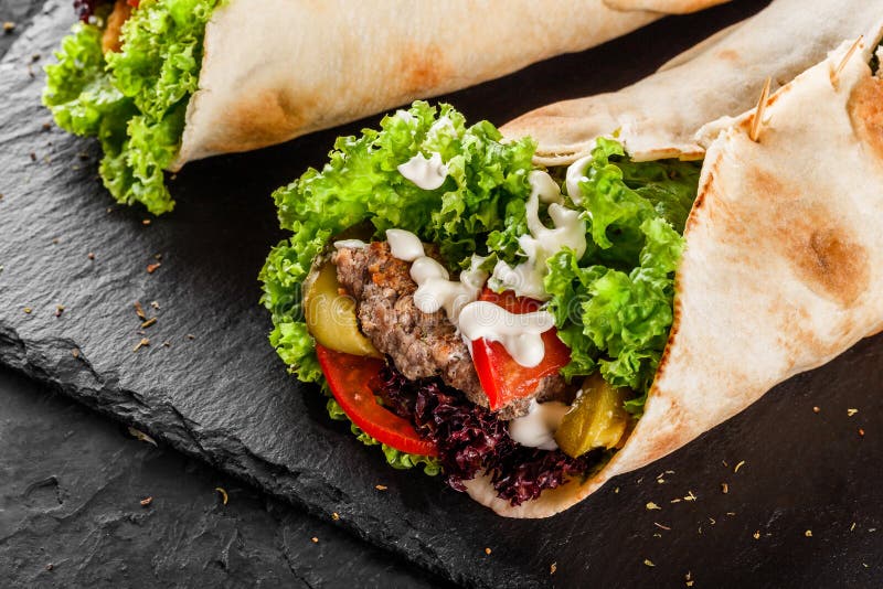 Tortilla wraps with grilled meat, fresh vegetables and salad on black stone background. Healthy snack or take-away lunch. Tortilla wraps with grilled meat, fresh vegetables and salad on black stone background. Healthy snack or take-away lunch.