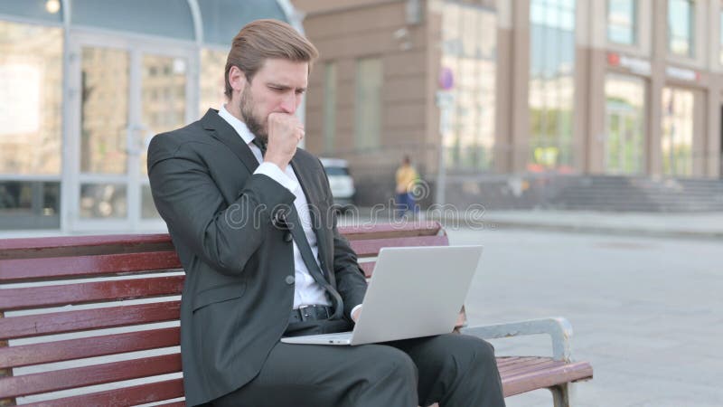 Toser a un hombre de negocios usando un portátil mientras se sienta al aire libre en el banco fotos de archivo