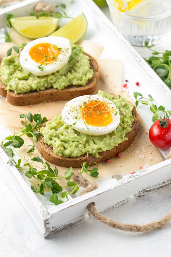 Tostada con pur? del aguacate y el huevo pasado por agua en la bandeja blanca, yema de huevo l?quida, desayuno delicioso, bocadil fotos de archivo Tostada con pur? del aguacate y el huevo pasado por agua en la bandeja blanca, yema de huevo l?quida, desayuno delicioso, bocadil fotos de archivo