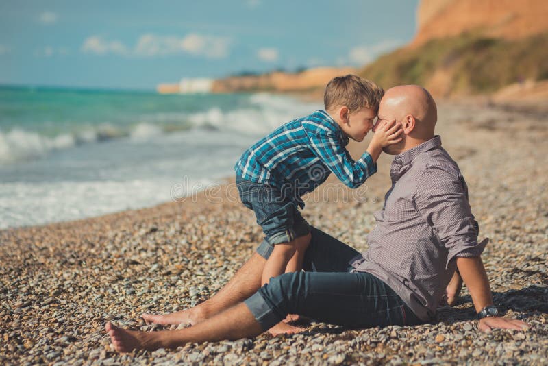 Touching appealing scene of father and son enjoy summer vacation together playing on stone beach wearing stylish shirt and fashion.