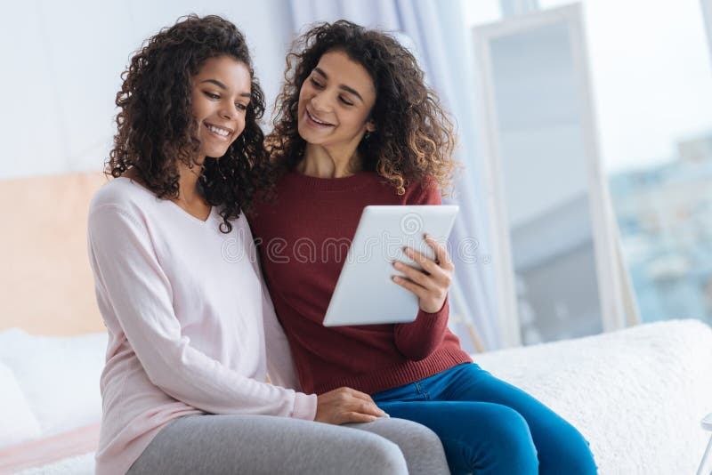 Touchpad curioso della tenuta della giovane signora e sorridere a sua sorella fotografia stock libera da diritti Touchpad curioso della tenuta della giovane signora e sorridere a sua sorella fotografia stock libera da diritti