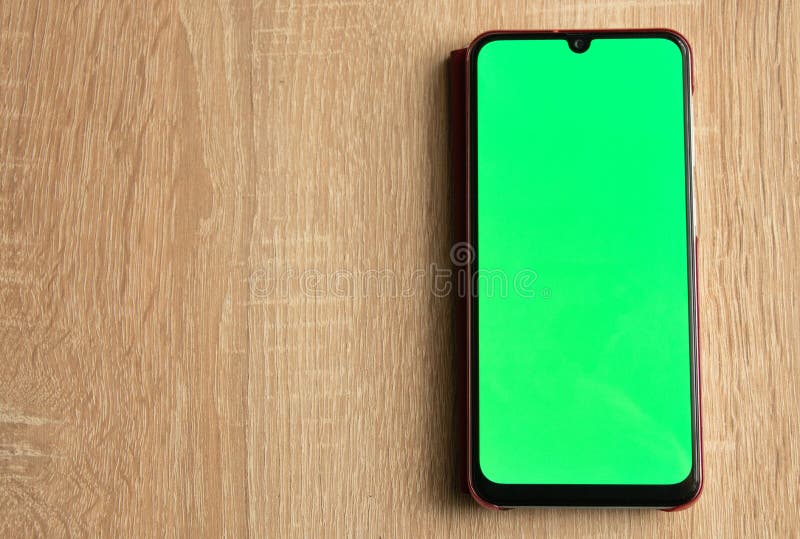 Handphone dengan green screen dipasang di atas meja kayu.