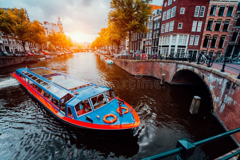 Tour boat at famous Dutch canal on sunset evening. Traditional Dutch bridges and medieval houses. Amsterdam Holland