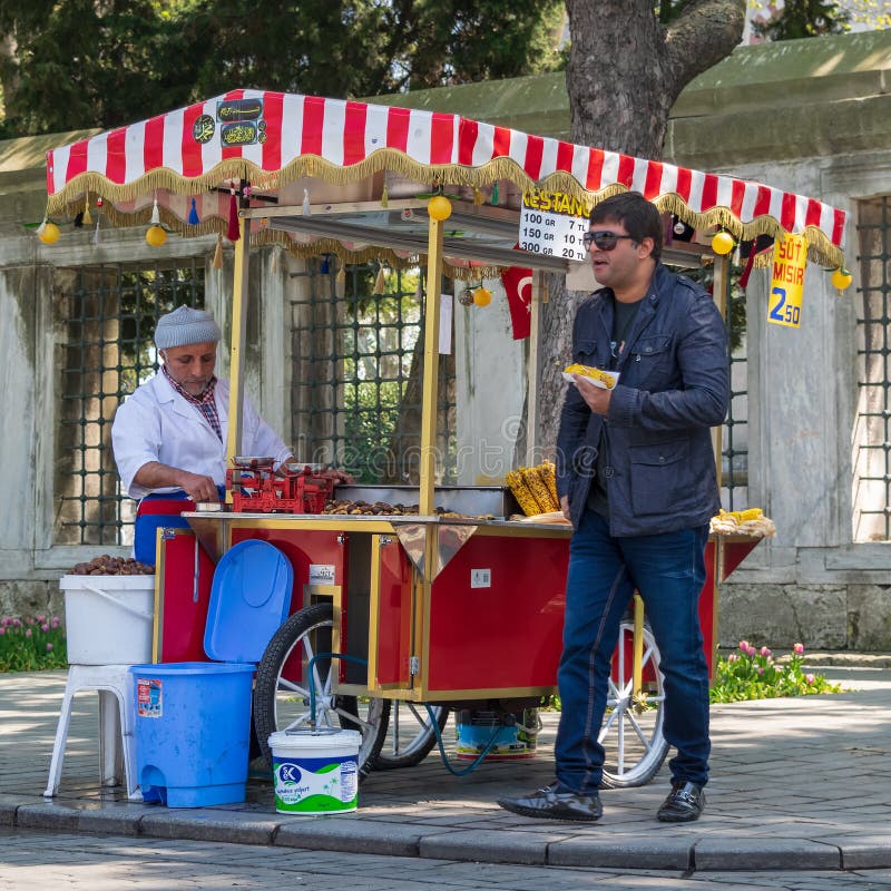 Istanbul, Turkey - April 16, 2017: Tourist buying fast food meal from a traditional Turkish chestnut and corn cart in Sultan Ahmed Square. Istanbul, Turkey - April 16, 2017: Tourist buying fast food meal from a traditional Turkish chestnut and corn cart in Sultan Ahmed Square