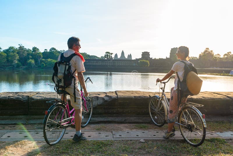 Tourist couple cycling in Angkor temple, Cambodia. Angkor Wat main facade reflected on water pond. Eco friendly tourism traveling royalty free stock images Tourist couple cycling in Angkor temple, Cambodia. Angkor Wat main facade reflected on water pond. Eco friendly tourism traveling royalty free stock images