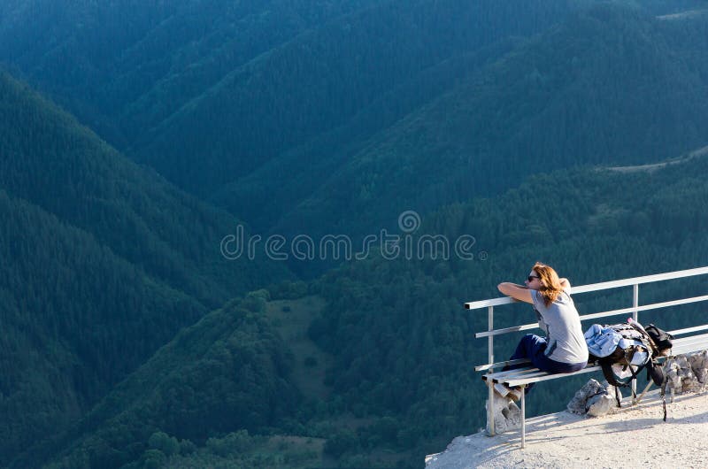 Femmina turistiche seduto su una panchina a godersi il panoramico con vista sulle montagne.